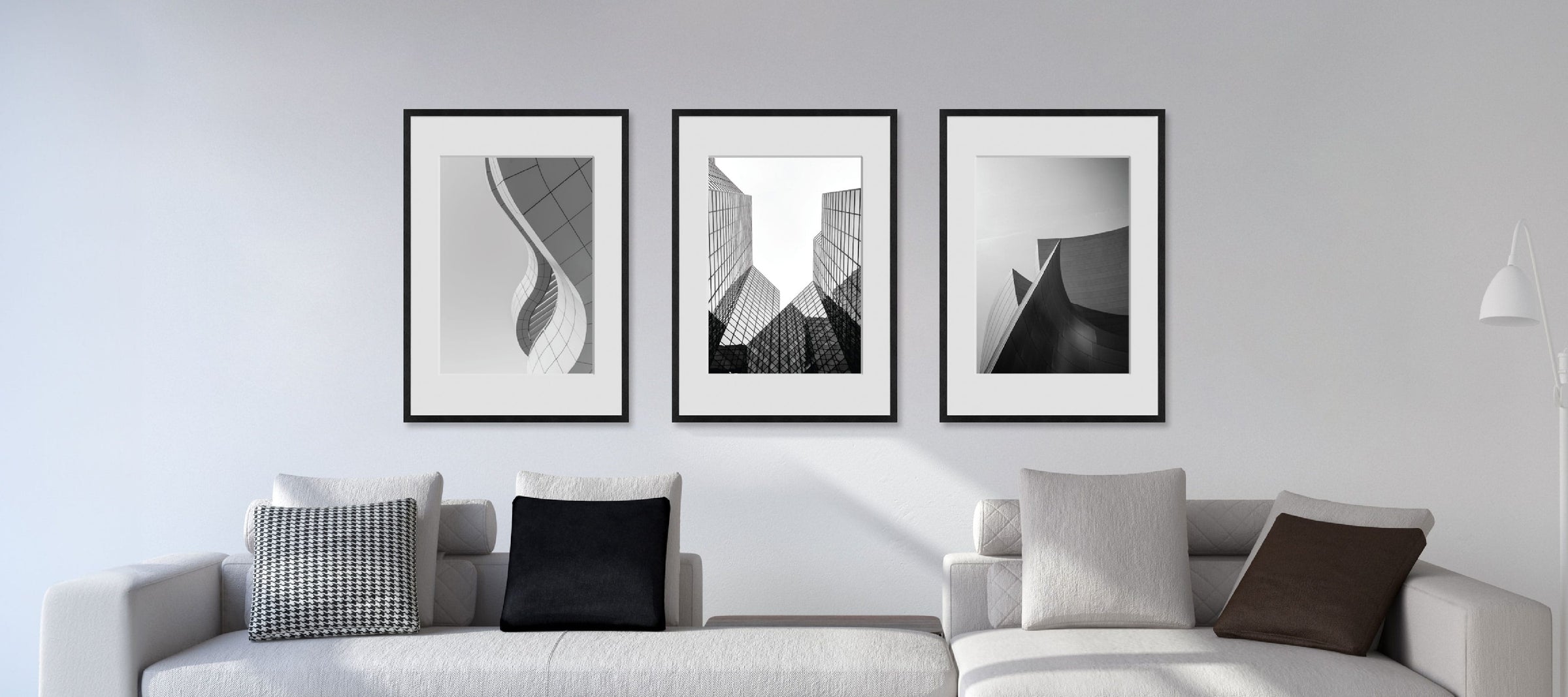 Gray sofa with decorative pillows and framed black and white artworks on a light gray wall.